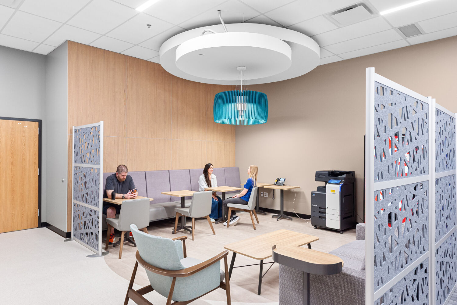 Teachers lounge with upholstered banquette seating, small meeting tables, lounge chairs, decorative privacy screens, pendant lighting, and a shared work counter.