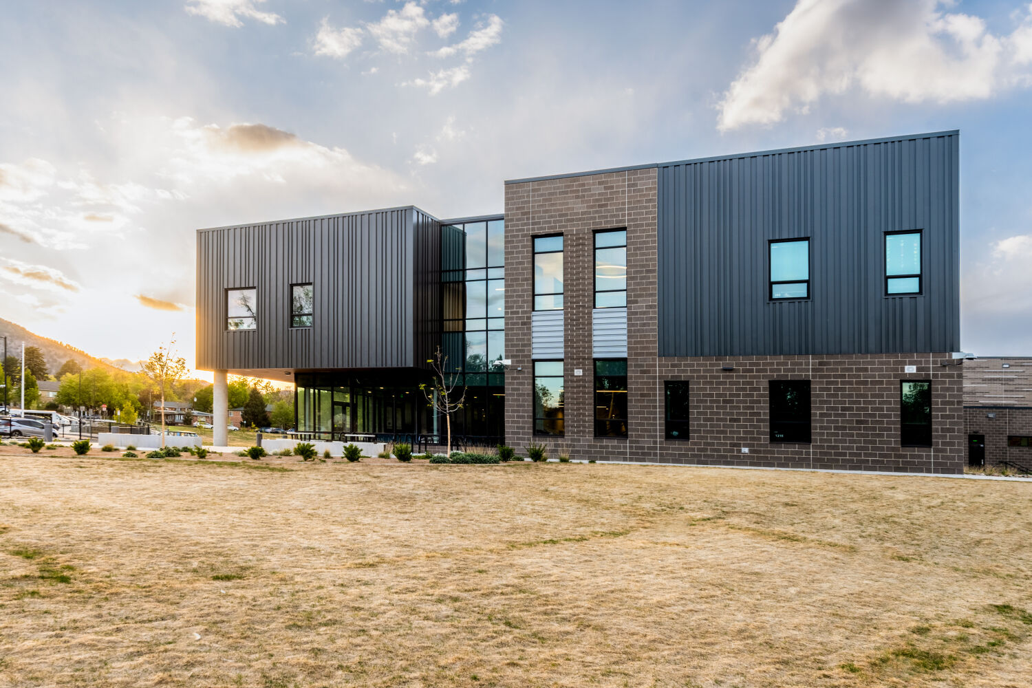 New Vista High School side elevation with a cantilevered metal-clad volume, brick base, vertical glazing at the entry, and landscaped lawn in the foreground.