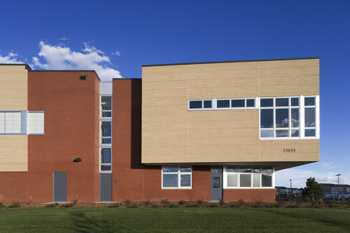 Exterior detail of Florida Pitt Waller School showing red and tan brick façades, narrow horizontal windows, cantilevered upper volume, and landscaped lawn under a clear sky.