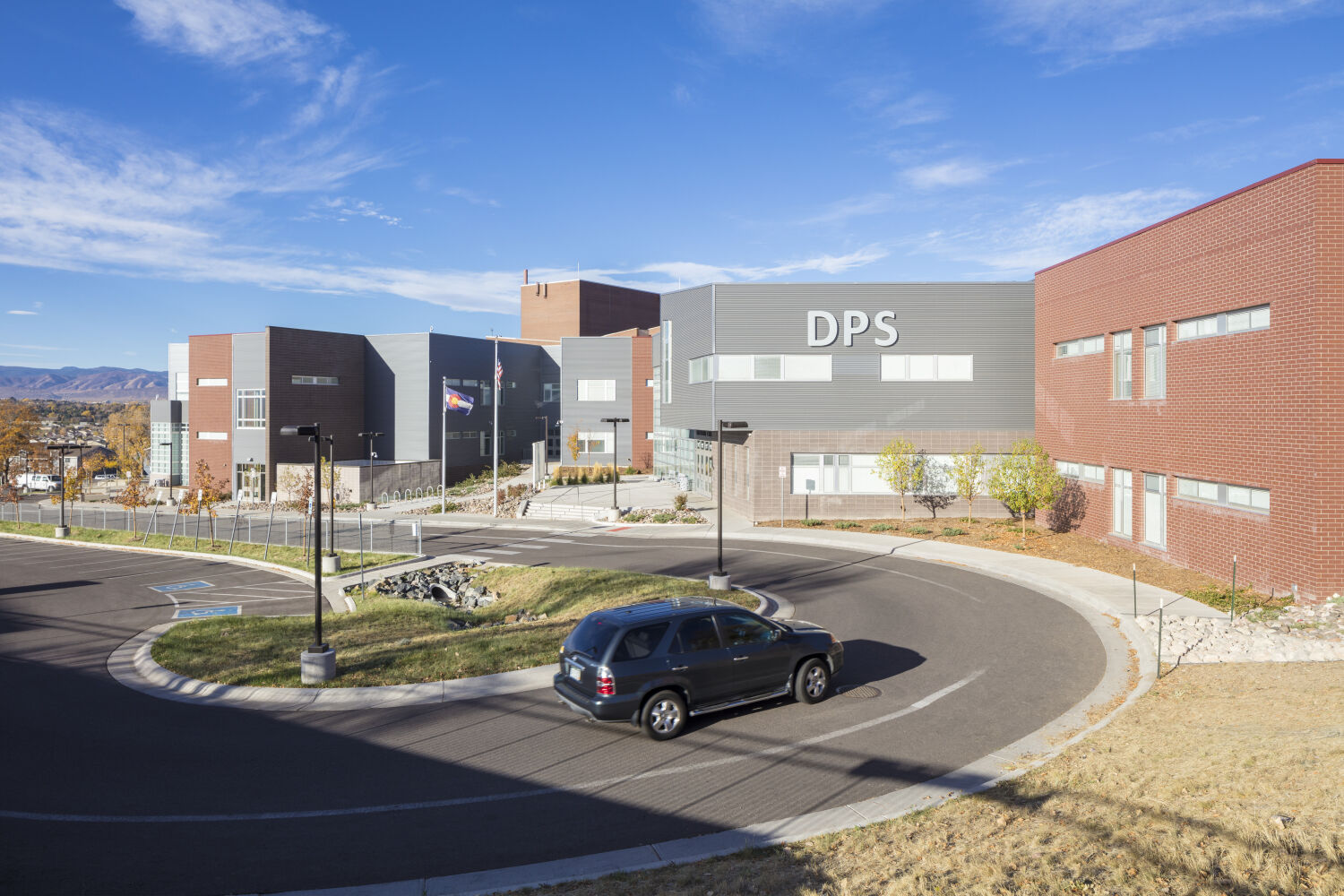 Exterior view of DSST College View Campus with red brick and gray metal‑panel façades, large windows, a circular drop‑off drive, landscaped areas, and mountain views in the background.