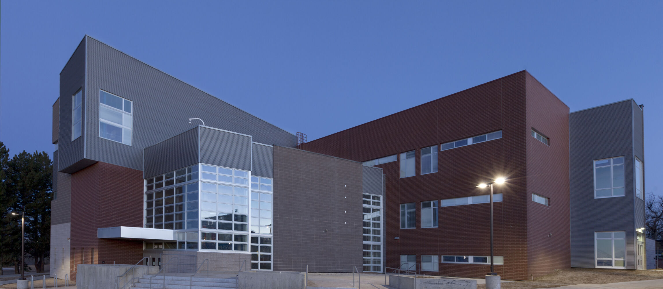 Exterior view of DSST College View Campus with red brick and gray metal‑panel façades, large glass window walls, and stepped concrete walkways.