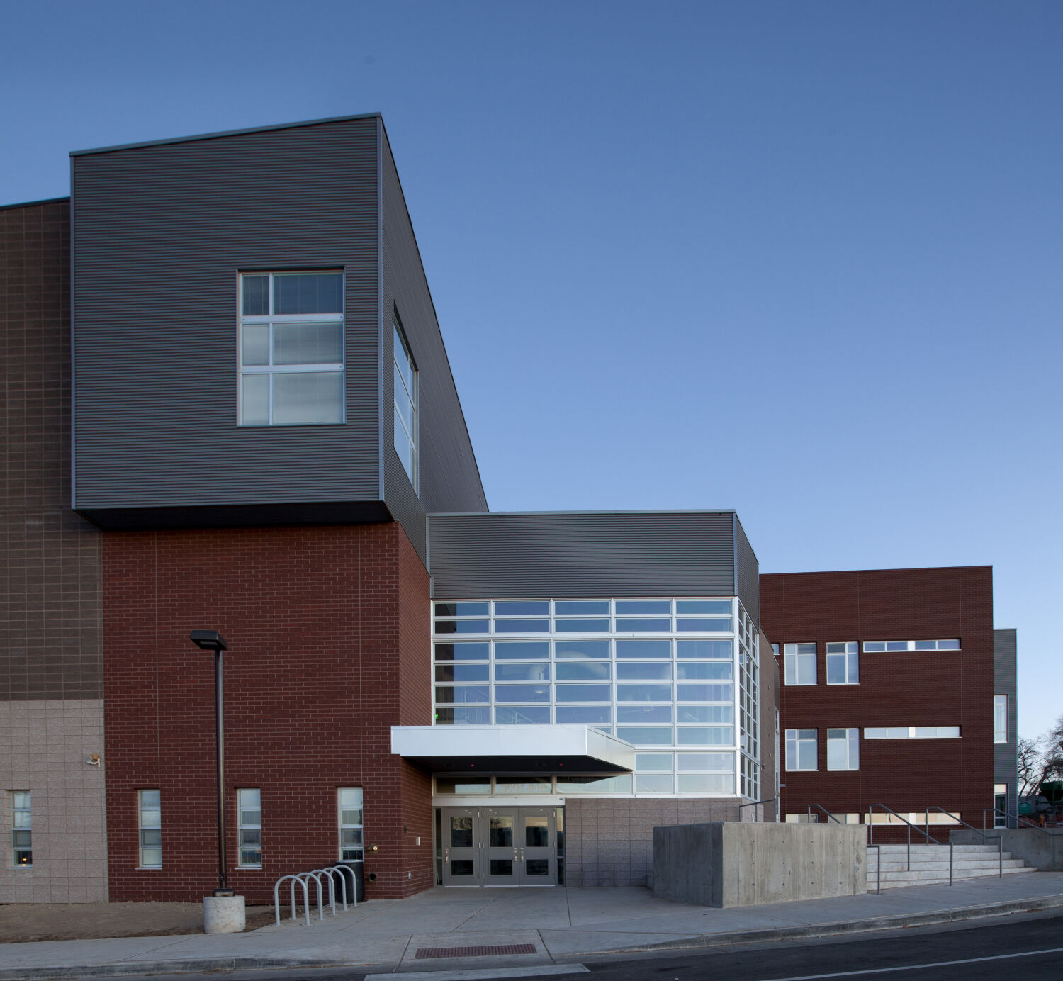 Exterior view of DSST College View Campus with a mix of red brick, tan masonry, and dark metal‑panel façades, large windows, and a recessed glass entry.
