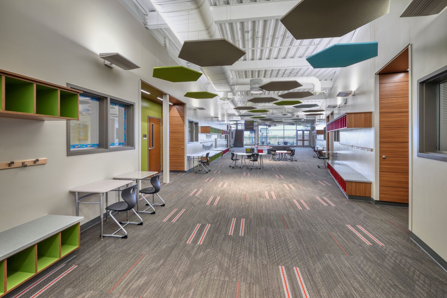 The Deer Trail PK–12 School learning commons with flexible seating, built-in storage cubbies, colorful ceiling panels, and large windows providing natural light.