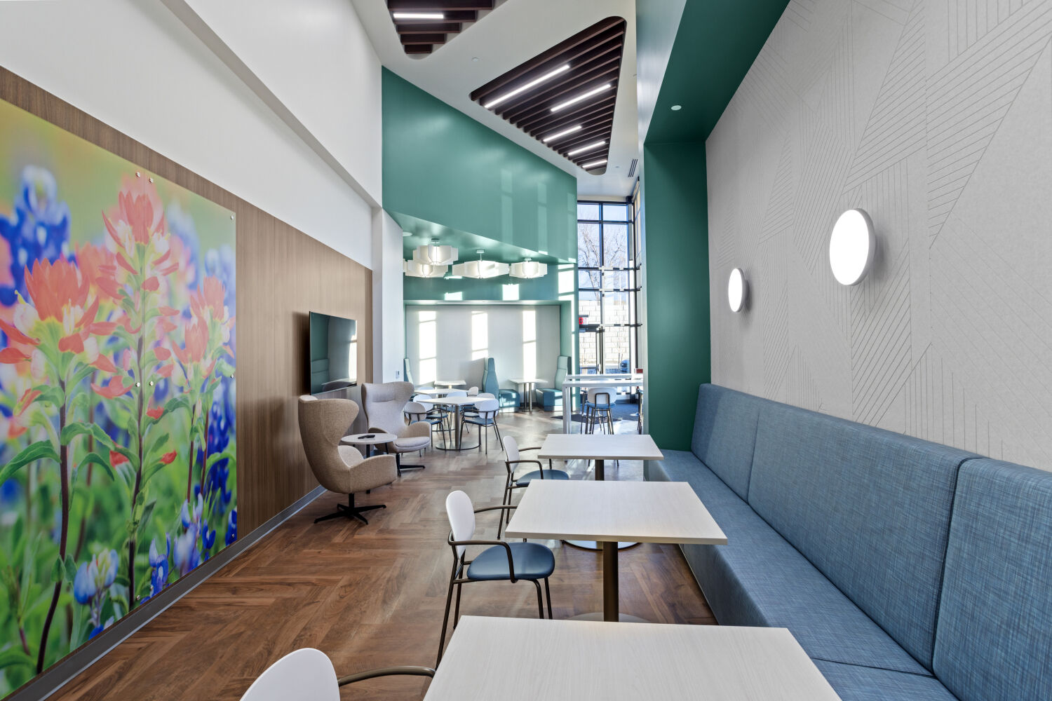 Staff lounge at the Casper–Natrona County Health Department with café tables, banquette seating, wood flooring, accent walls, and pendant lighting.