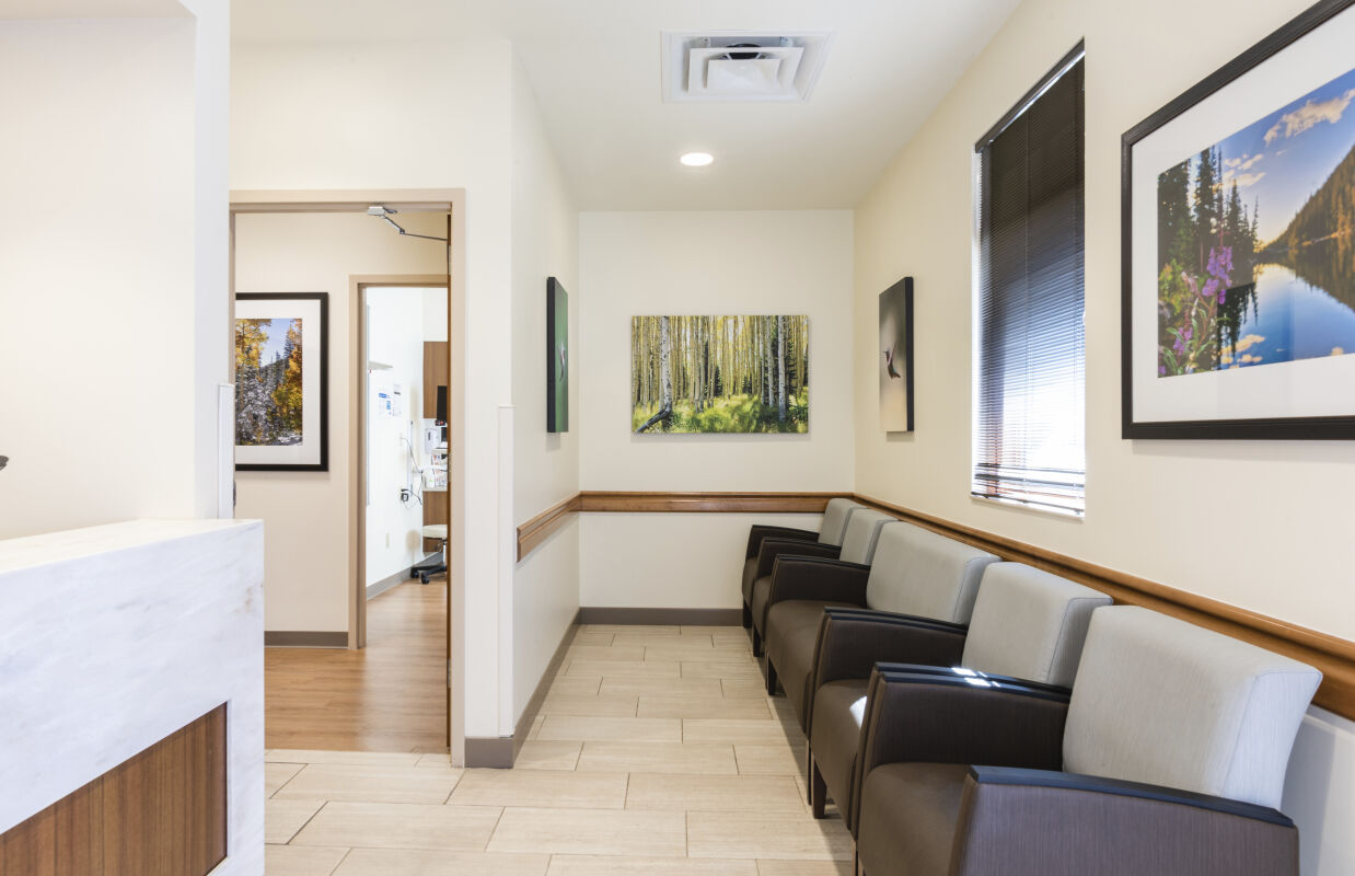Waiting area with rows of upholstered chairs, framed nature photography on the walls, tile flooring, and a view into an adjacent corridor and exam room.