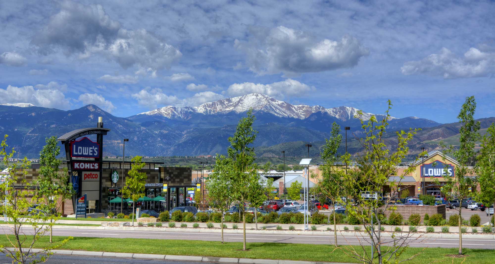 A snow-capped Pikes Peak mountain in the background of the University Village shopping center buildings.