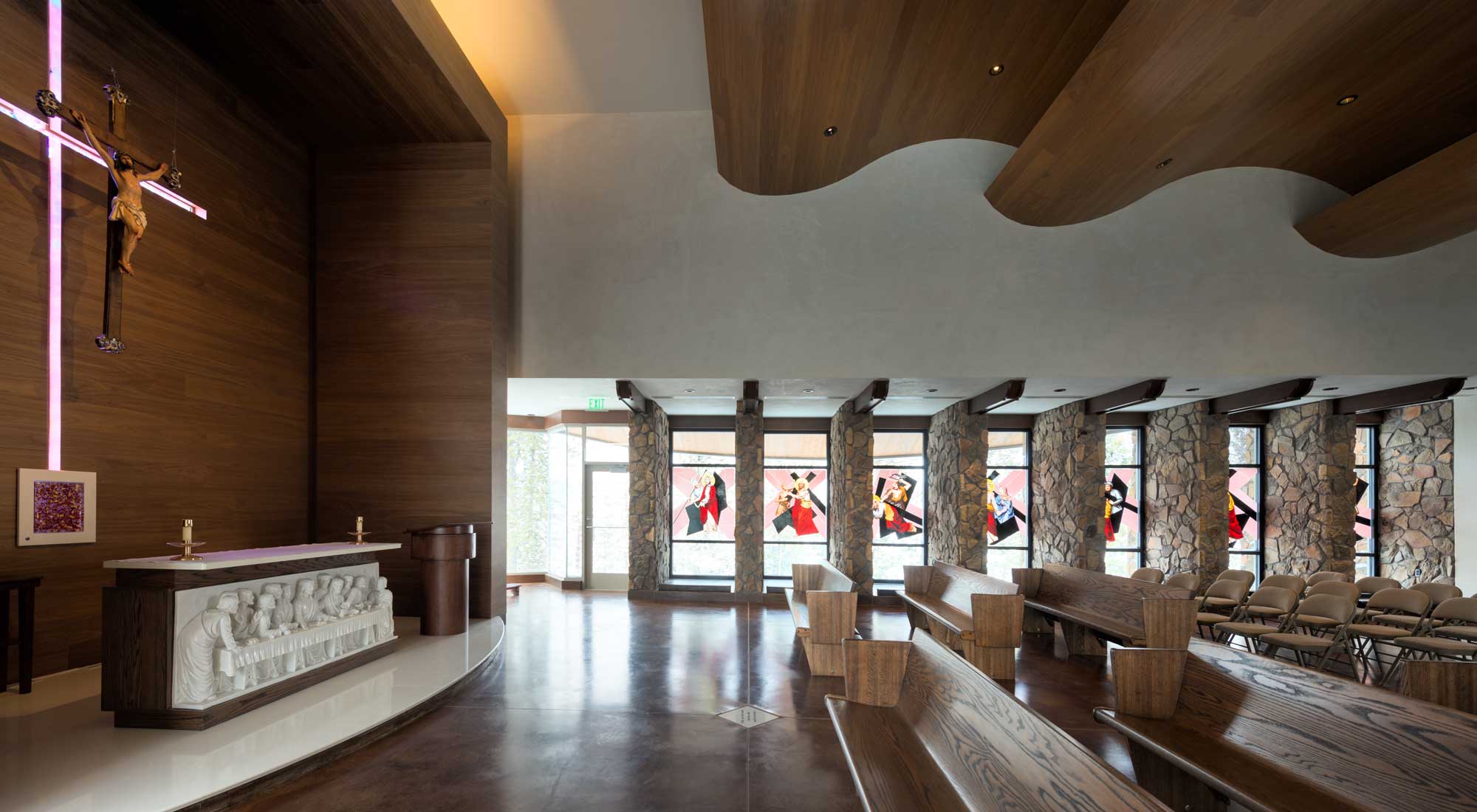 Interior view of the Chapel at El Tesoro, featuring a serene altar with a large wooden cross, natural stone accents, and soft lighting. Wooden pews are arranged neatly, creating a warm and inviting worship space.