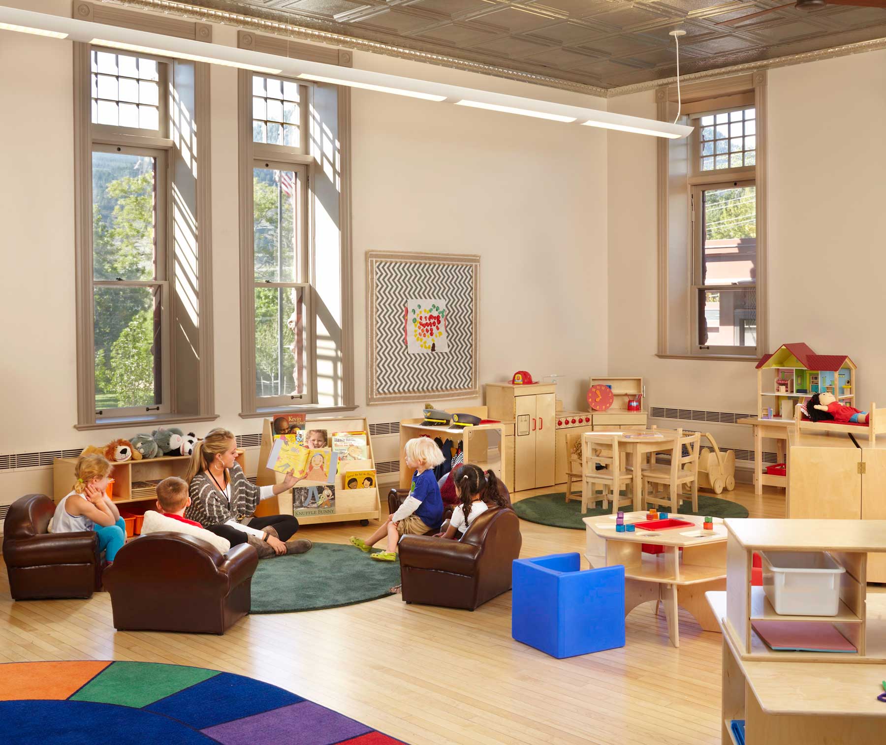 Four young children sitting in a circle while listening to a teacher read from a book.