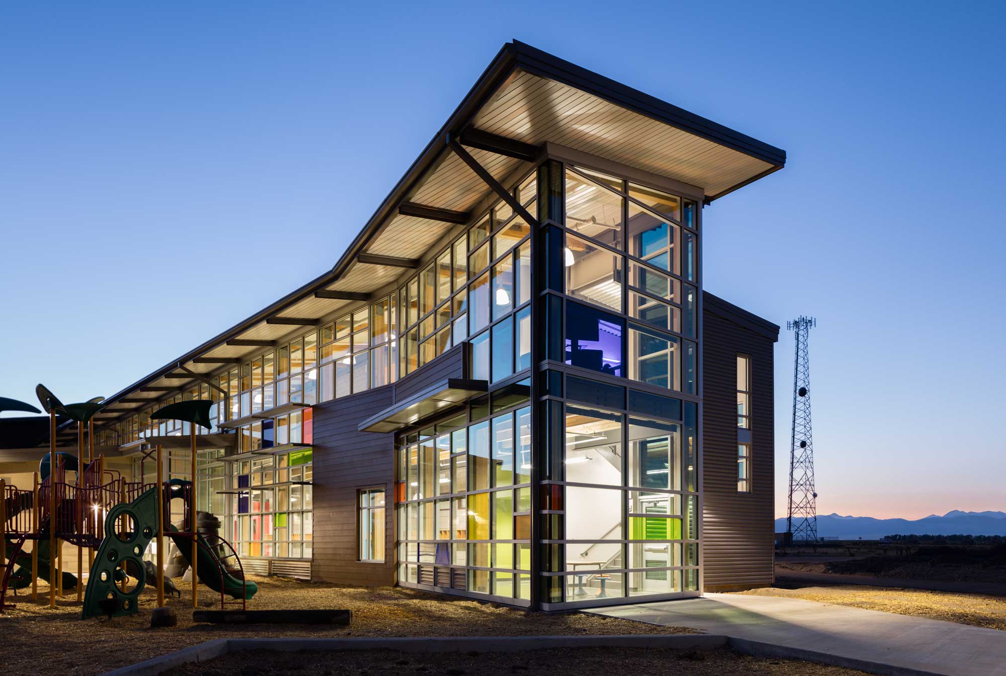 Side view of Moffat School, highlighting its modern architecture with clean lines, large windows, and a mix of metal and brick materials. The building is set against a backdrop of an open sky and grassy surroundings.