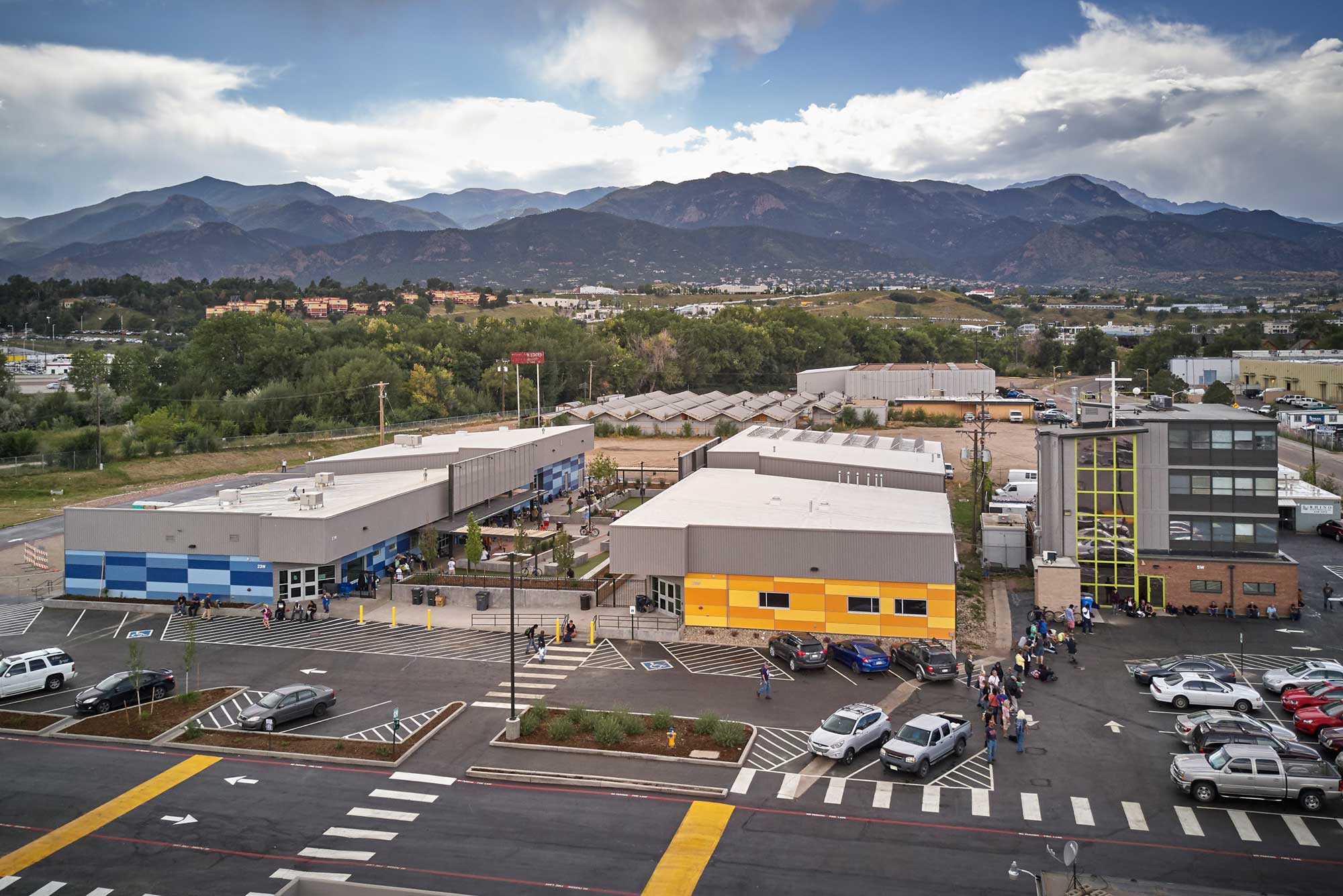 Exterior view of the SRM complex, featuring a modern multi-building design with large glass windows, wood and metal accents, and well-maintained landscaping. The setting is surrounded by open space under a partly cloudy sky.