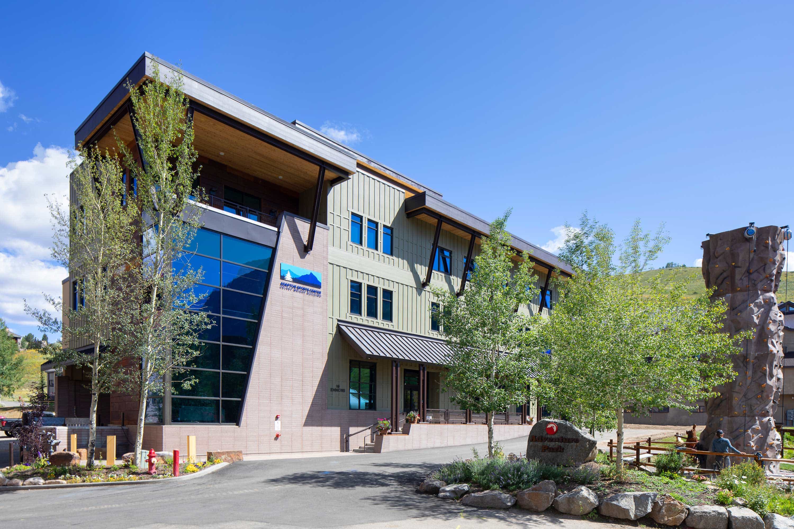 Exterior view of the Adaptive Sports Center, showcasing a modern design with large windows, wood and metal accents, and a welcoming entrance. The building is set against a scenic backdrop, emphasizing accessibility and inclusivity.