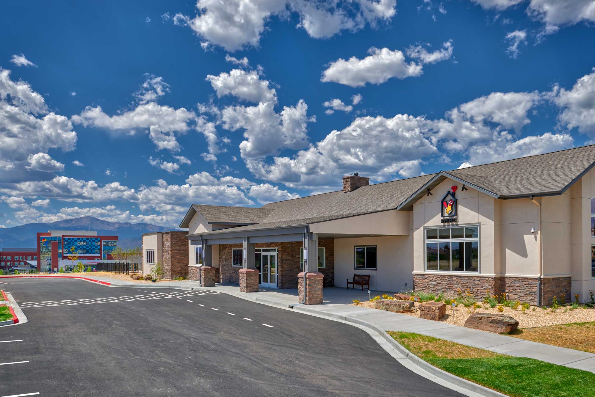 Exterior view of the Ronald McDonald House entrance, showcasing a welcoming design with warm-toned materials, large windows, and a covered entryway. Thoughtful landscaping enhances the inviting and home-like atmosphere of the building.
