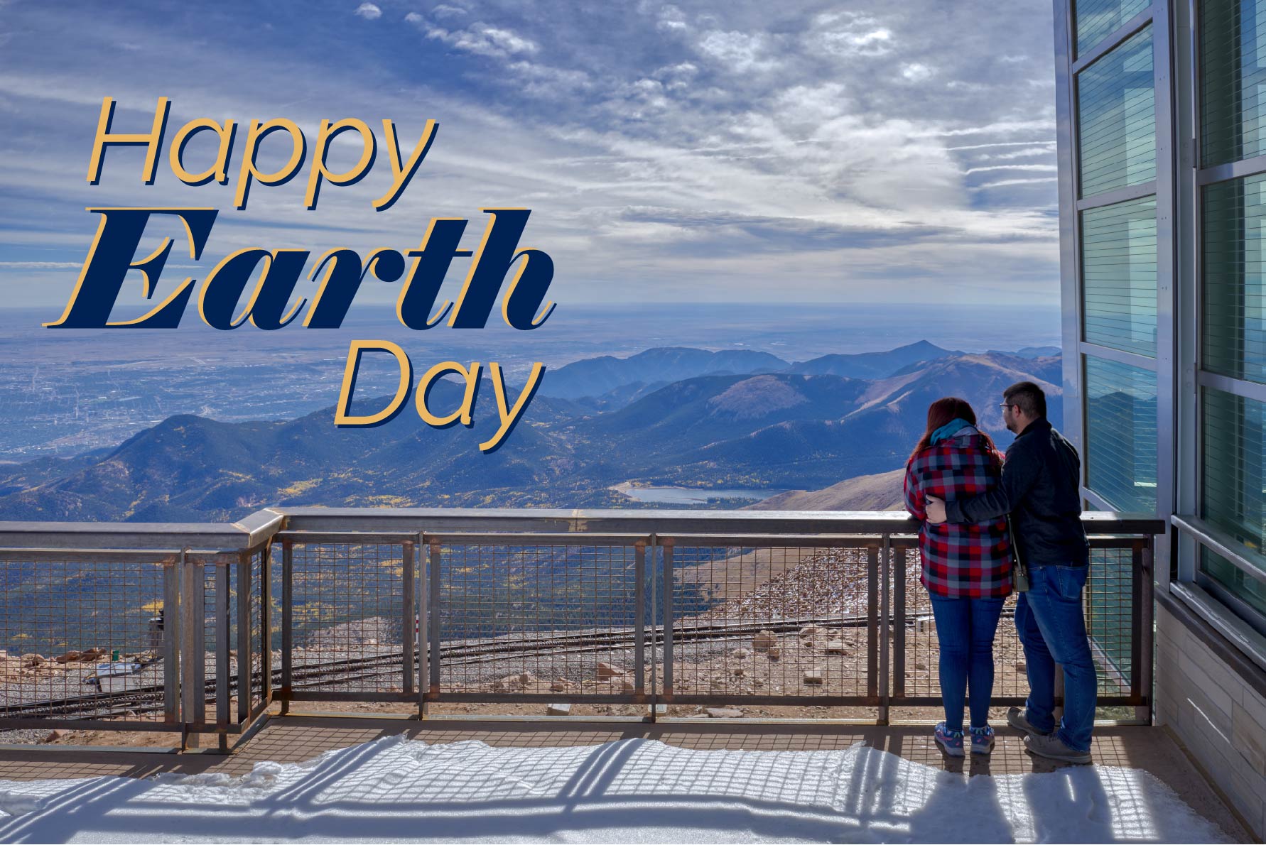 a couple stand on the Pikes Peak visitor center patio facing the view of mountains seen from atop Pikes Peak