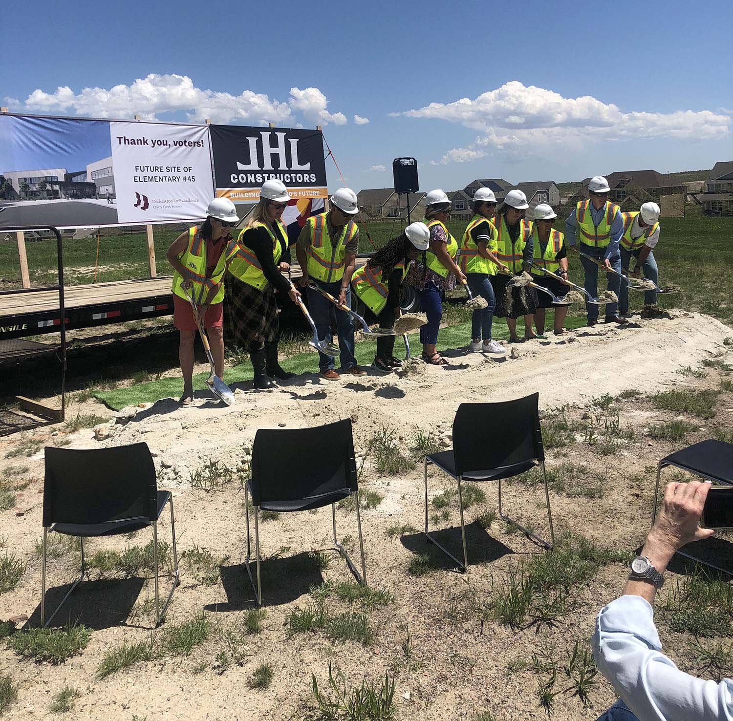 a group of adults in hardhats participate in the groundbreaking ceremony